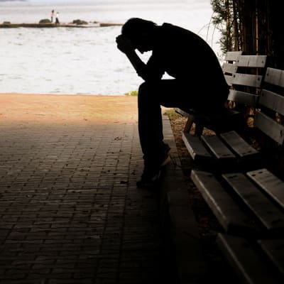 En pojke sitter på en parkbänk och lutar huvudet i händerna.