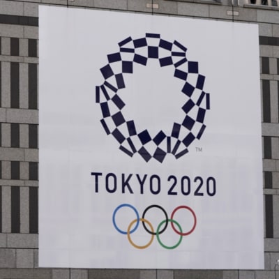 Person med ansiktsmask tittar på plakat med OS-logon.