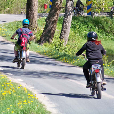 Mopedister kör efter varandra på en asfalterad väg.