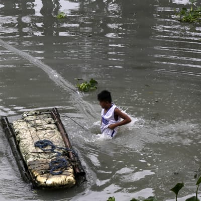 En filippinsk pojke leder en provisorisk flotte i ett översvämmat område i södra Manila.