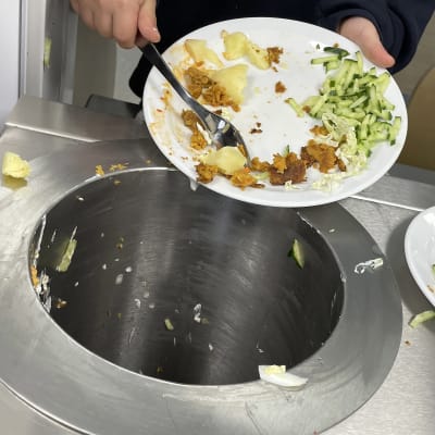 Lapsi  siirtää haarukalla ruoantähteitä lautaselta jäteastiaan.