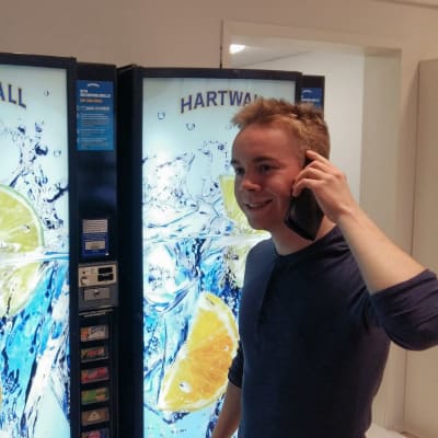 Gymnasieeleven Rasmus Östdahl står med telefon i hand och beställer läsk från en varuautomat i skolan.
