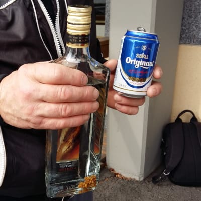 En man håller en vodkaflaska i ena handen och en ölburk i den andra.