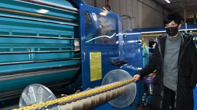 En kvinna står bredvid en maskin som används inom textilindustrin i en fabrikshall.