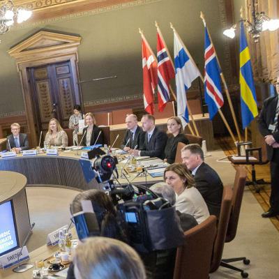 Nordiska ministrar samlade kring mötesbord medan fotografer fotograferar dem.
