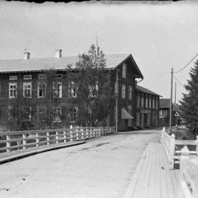 Mustavalkokuva, jossa Kosolan talo 1900-luvun alkupuolella Lapuanjoen rannalla sillan vieressä.