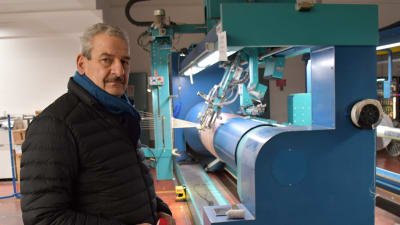 En man står framför en maskin som används vid tillverkningen av tyger och garn.
