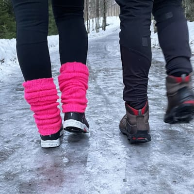 Två par fötter i närbild, utomhus på en isig väg, går bort från kameran.