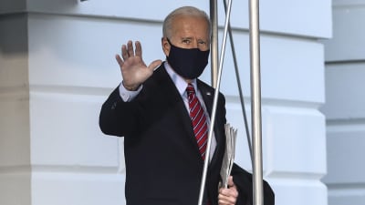 Gråhårig man i kostym och munskydd vinkar åt kameran. President Joe Biden utanför Vita huset den 5 februari 2021, på väg till Wilmington i Delaware.