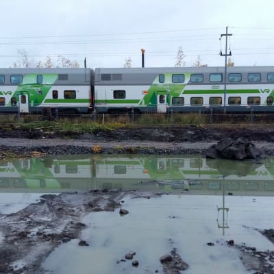 VR:s grönvita tåg speglas i en vattensamling längs Kustbanan.