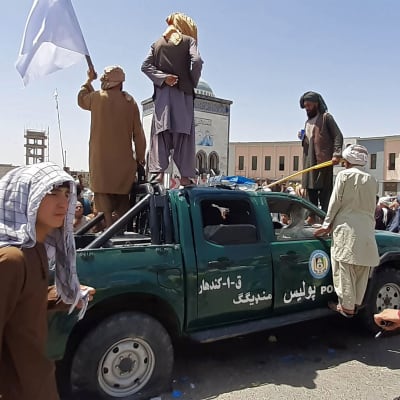 Taleban -taistelijat seisovat vaurioituneen poliisiauton päällä.