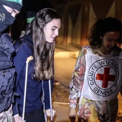 Maya Regev (i mitten) var en av dem som kidnappades från musikfestivalen Supernova den 7 oktober och som frigavs på lördagen. Hon skadades i foten i samband med kidnappningen. Här omges hon av en medlem av Hamas väpnade gren och en person från Internationella Rödakorskommittén. 