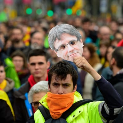 En demonstrant håller upp en pappersmask av Carles Puidgemont i Barcelona den 25 mars 2018.