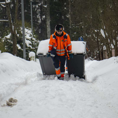 Jäteauton kuljettaja vetää roska-astioita lumimössössä.