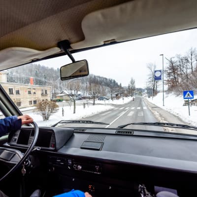 Händer på en ratt i en lastbil och vy över ett vintrigt landskap och väg genom fönsterrutan.