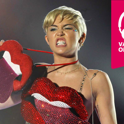 Miley Cyrus grimaserar och håller upp en stor konstgjord mun som har tungan utsträckt.
