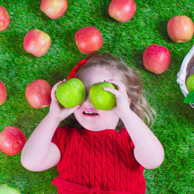 En flicka omringad av gröna och röda äppel.