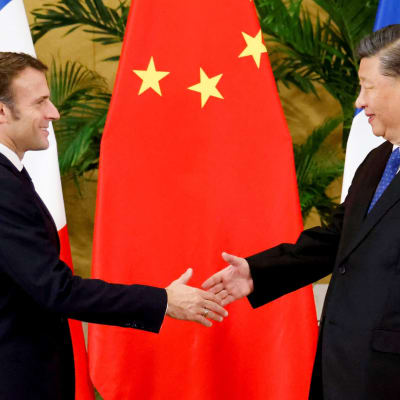 Puolikuvassa kaksi pukuun pukeutunutta ihmistä kättelee. Taustalla Kiinan ja Ranskan liput. 