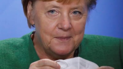 Angela Merkel håller på att sätta på sig ett munskydd.