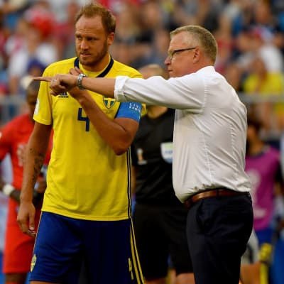 Janne Andersson i vit skjorta förklarar saker för sin gulklädda spelare Andreas Granqvist.