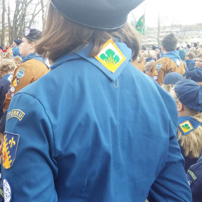 Scouter i olika färgers scoutriggar och baskrar står utanför Åbo Domkyrka inför scoutparaden.