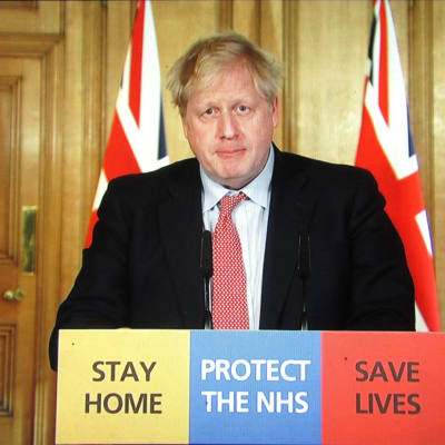 Boris Johnson tiedotustilaisuudessa 25. maaliskuuta 2020. Johnsonilla on todettu koronavirustartunta, ja lieväoireisen pääministerin kerrotaan jatkavan töitä eristyksestä.