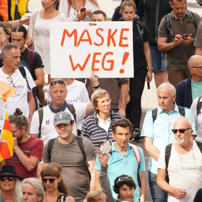 Folkmassa som demonstrerar. Det syns ett paraply och en skylt med tysk text.