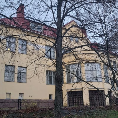 Ljusgul herrgård i trädgård på hösten.