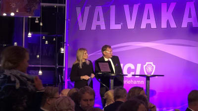 Valanalytiker och publik i violett belysning på valvakan i Mariehamn.