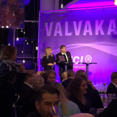 Valanalytiker och publik i violett belysning på valvakan i Mariehamn.
