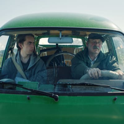 Stefan (Martin Paul) och Nisse (Peik Stenberg) sitter tillsammans i en grön paketbil. 