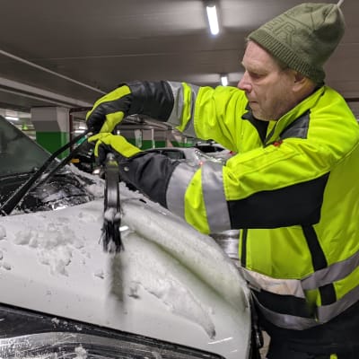 Jyrki Lieto putsaa autoaan lumesta Itäkeskuksen Prisman parkkihallissa.