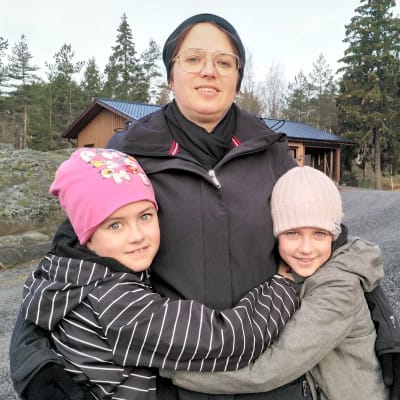 En mamma som omfamnas av sina två döttrar.