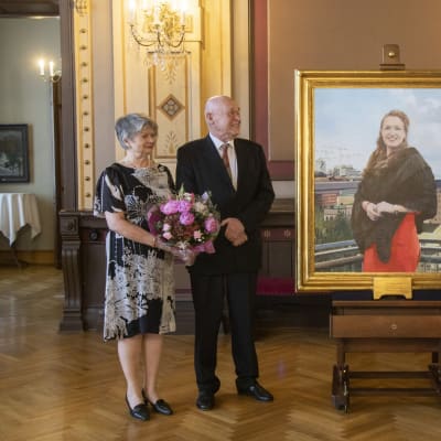 Taiteilija Timo Vuorikoski seisoo vaimonsa kanssa Anna-Kaisa Ikosta esittävän teoksen vieressä. Teoksen oikealla puolella seisoo Anna-Kaisa Ikonen.