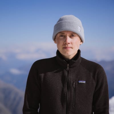 Antti Koskinen seisoo ja katsoo kameraan. Taustalla sumea vuoristomaisema.