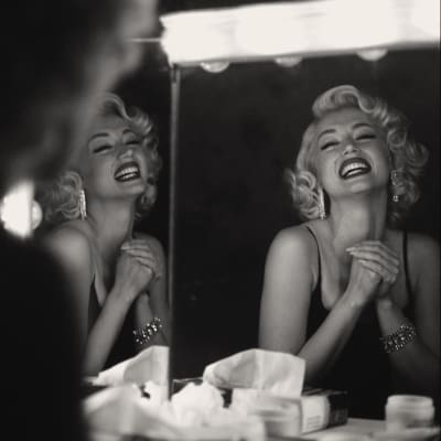 Svartvit bild där vi ser Marilyn Monroe (Ana de Armas) som sitter vid en spegel och skrattar ansträngt.