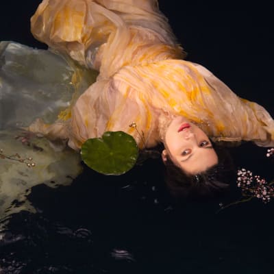 En mörkhårig kvinna som ligger i vattnet bland näckrosblad.