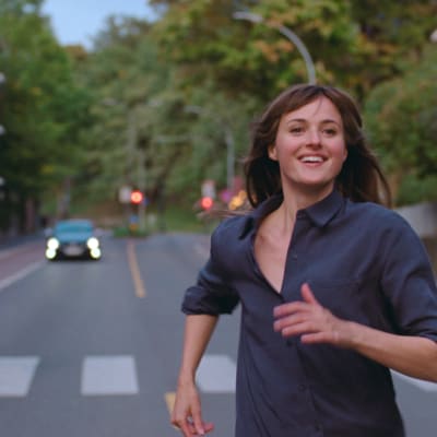En kvinna springer leende mitt på en bred gata i en stad.