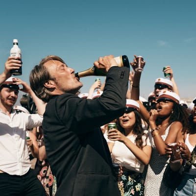 Martin (Mads Mikkelsen) dricker direkt ur en champangeflaska medan unga studenter jublar runtom honom.