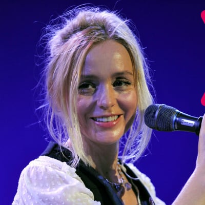 Lisa Ekdahl ler med öppen mun och håller med ena handen i en mikrofon som är i en mikrofonställning.