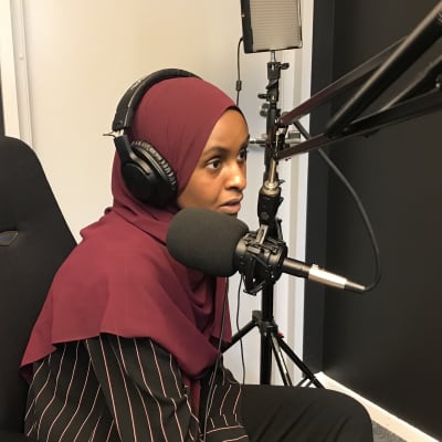 Ung kvinna med hijab och hörlurar i en poddstudio.