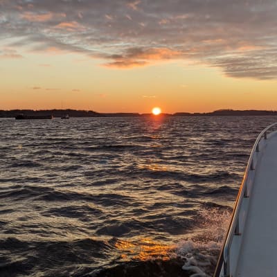 Aurinko nousee Suomenlahden ylle. Kuvan reunassa näkyy veneen seinää.