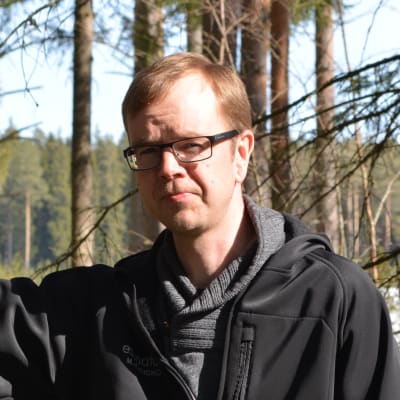 Biolog och naturföretagaren Mattias Kanckos lutar sig mot en tall i en gles skog. Vårsolen skiner och det finns en del snöfläckar ovanpå lingonriset i bakgrunden. 