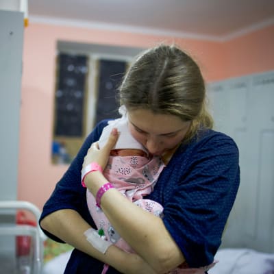 En kvinna håller i en nyfödd bebis i famnen.