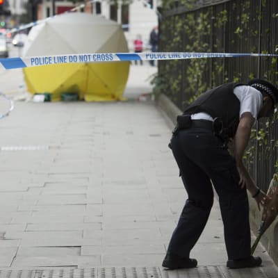 En polisman lägger en blombukett vid platsen för knivdådet i London.