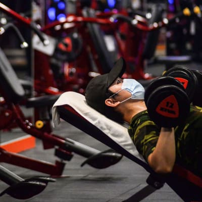 En man i munskydd lyfter vikter på ett gym.
