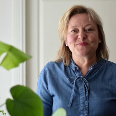 Tina Landén står invid en byrå med en grön växt.
