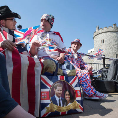 tre män i kläder prydda med storbritanniens färger blått, rött och vitt sitter framför Windsor slott