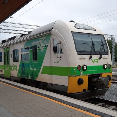 Vihreänvalkoinen juna pysähtyneenä rautatieasemalle.