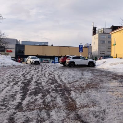 En relativt tom parkeringsplats. Det är is och sand på marken. I bakgrunden syns Lundi-huset.